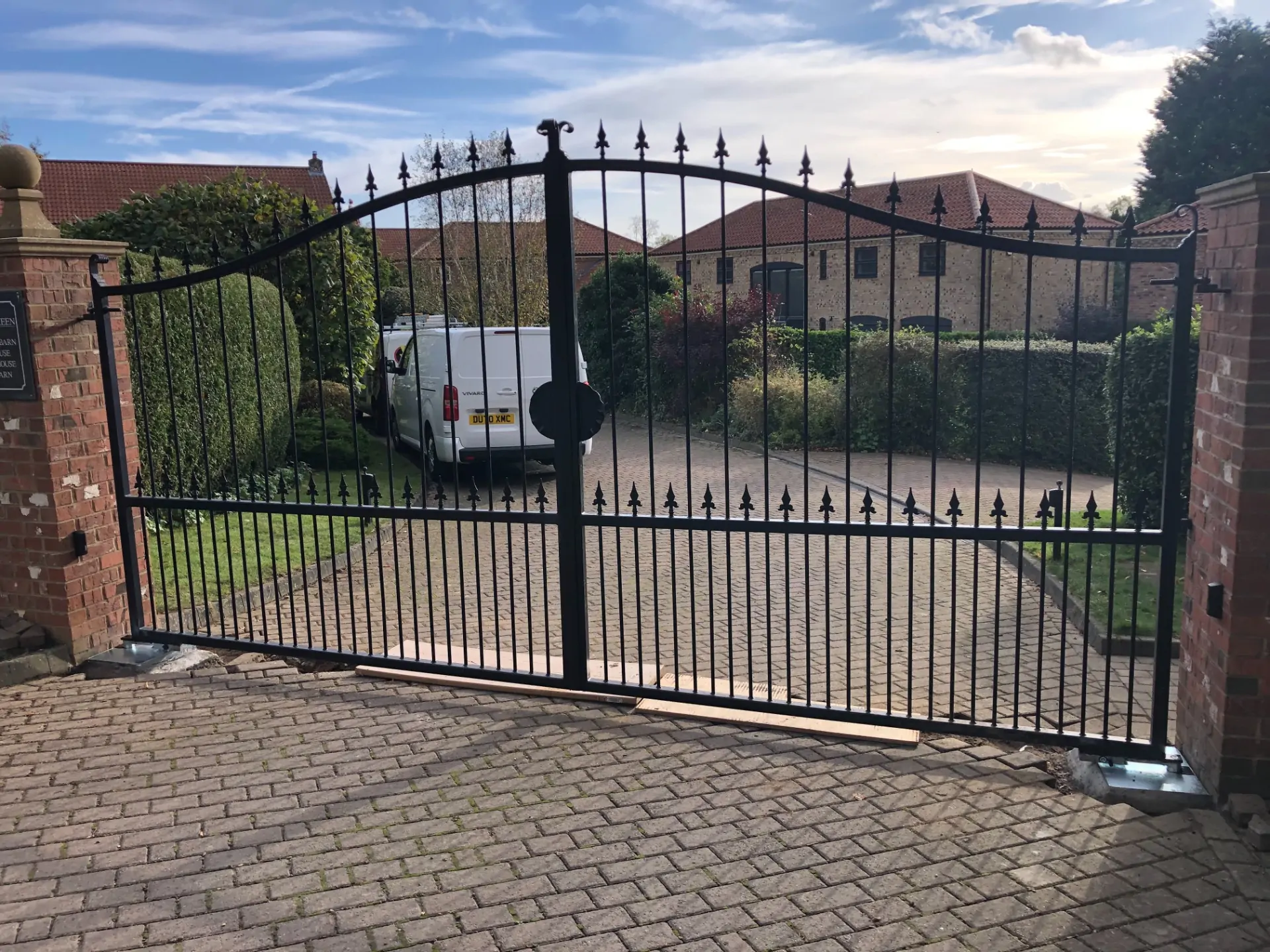 a black wrought gate with a brick wall and brick driveway